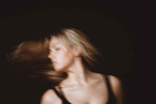 Woman in black tank top tossing blonde hair. Picture has a solid black background.